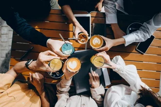 俯視圖顯示人們在戶外木桌上將各種冰熱咖啡飲料碰杯。