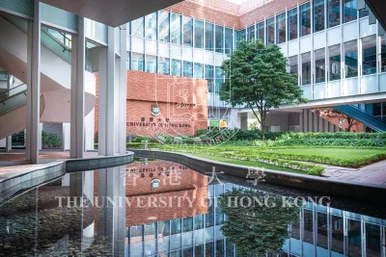 現代化校園庭院，映照池水面倒影著刻有香港大學校徽及名稱的紅磚牆，四周環繞著玻璃幕牆大樓、樹木及綠色草坪。
