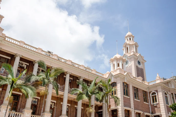 Exterior of HKU Main Building featuring colonial-style red brick facade, white columns, and clock tower under blue sky.