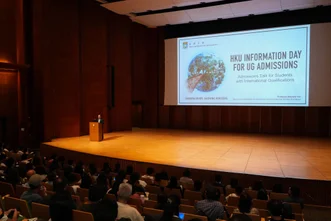 講者於大禮堂講台上主持講座，投影幕顯示「HKU INFORMATION DAY FOR UG ADMISSIONS」投影片，台下座無虛席。