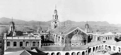 俯瞰香港大學本部大樓建築群及鐘樓的歷史黑白照片，背景為維多利亞港及山丘。