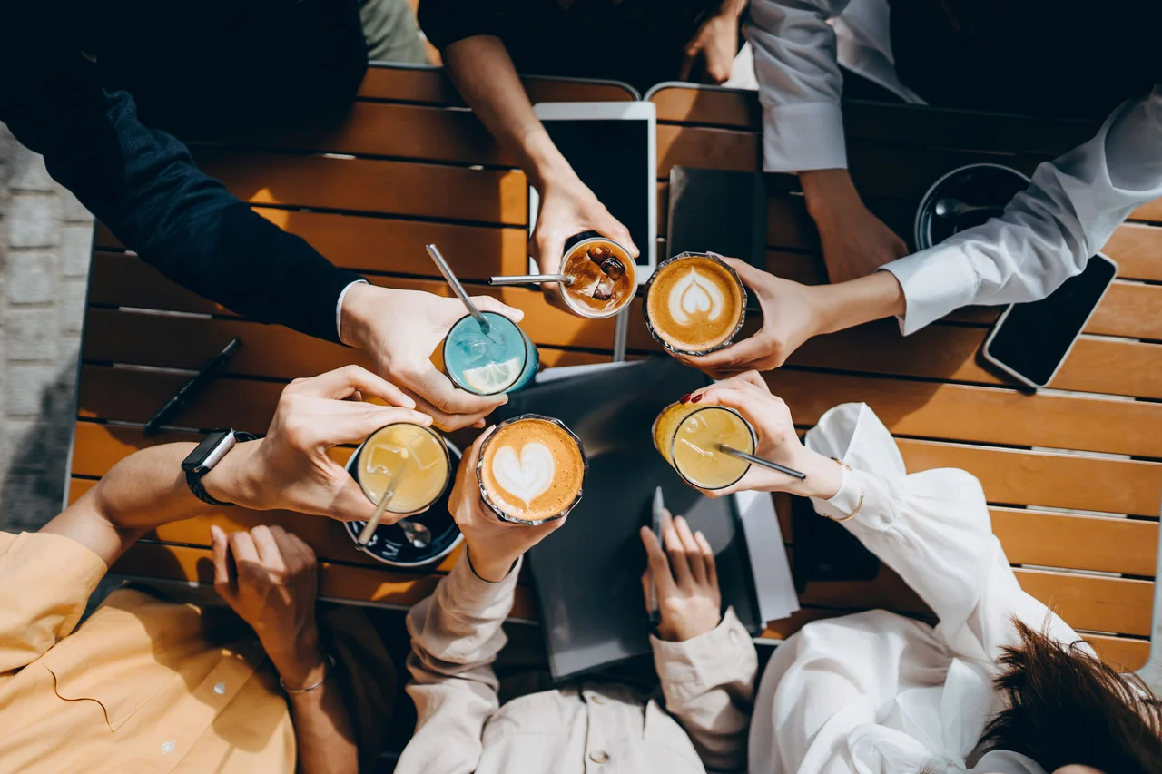 俯視圖顯示人們在戶外木桌上將各種冰熱咖啡飲料碰杯。